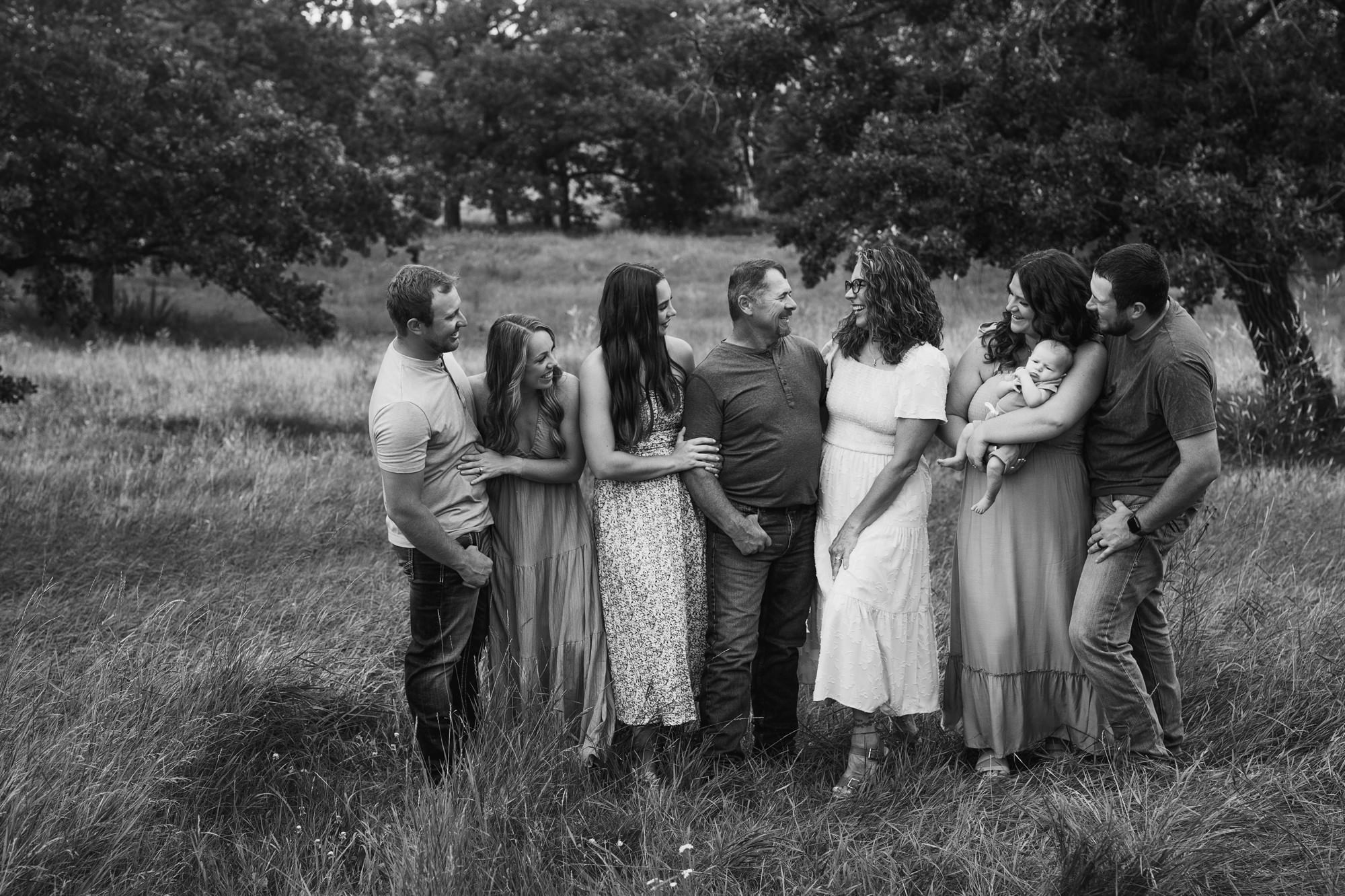 Black and white candid of a extended family laughing together during outdoor family pictures.