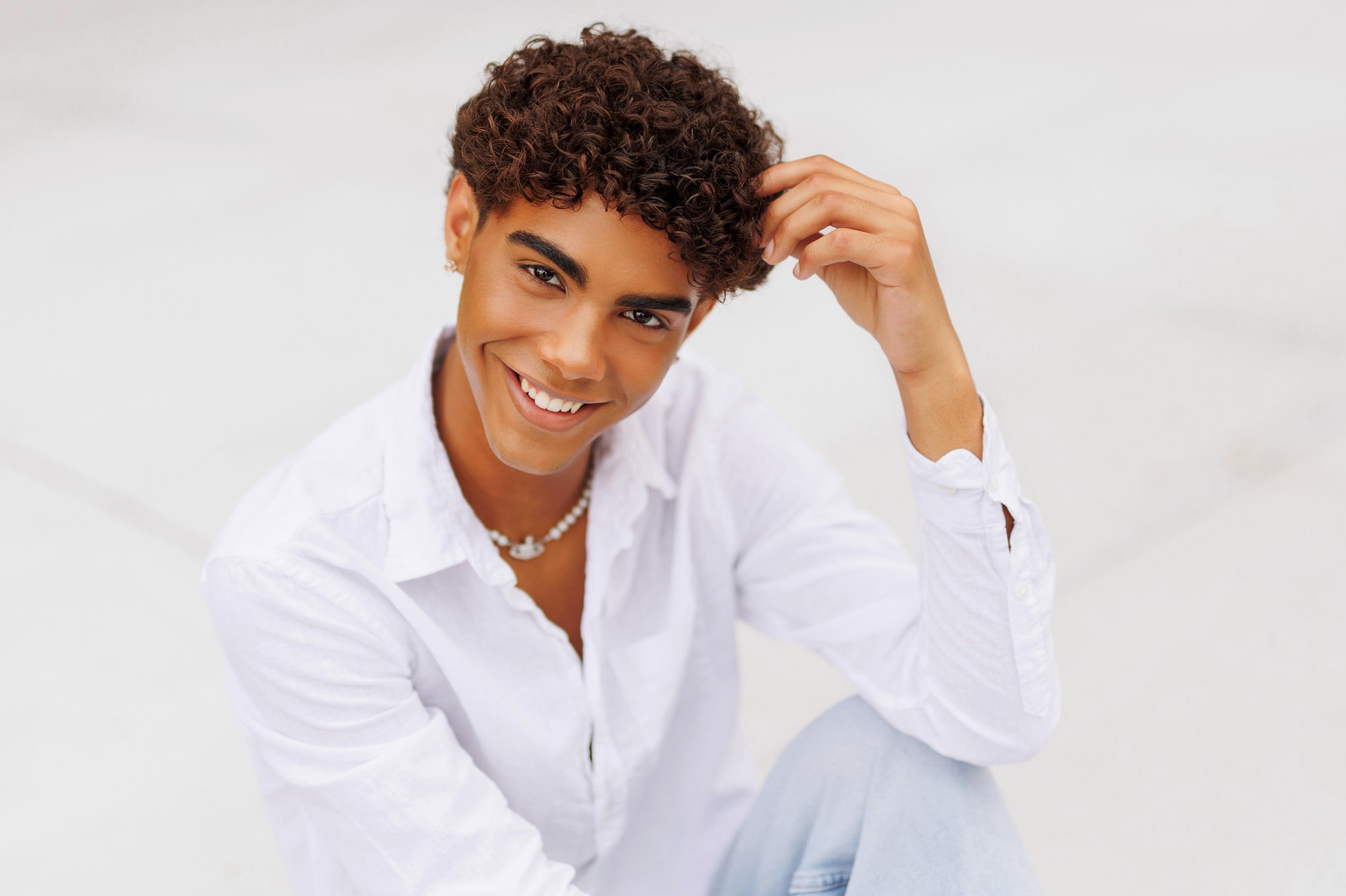 Monochromatic senior photo of guy in white shirt sitting against a crisp white background
