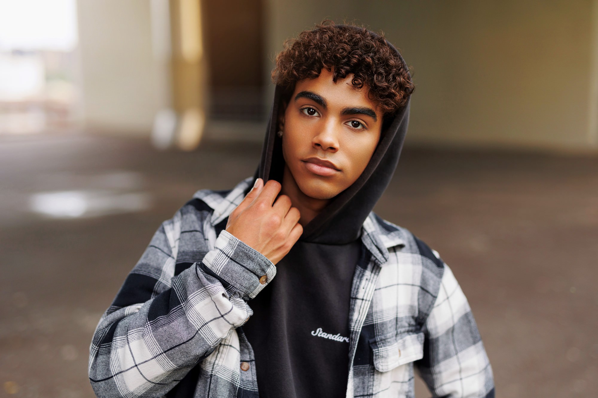 Urban senior portraits of curly haired senior boy wearing a hoodie standing under a minneapolis overpass